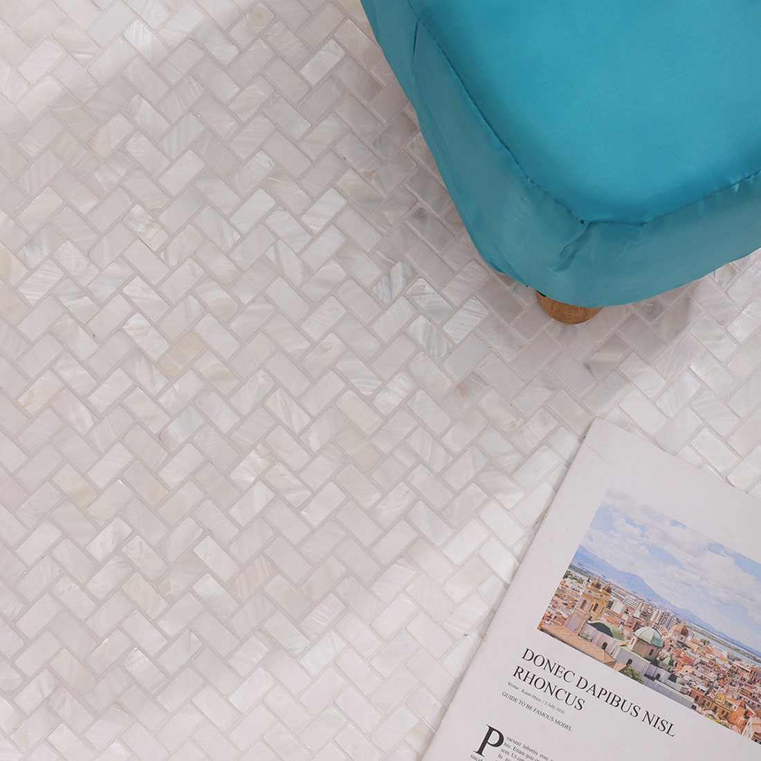 Styled scene showing herringbone mosaic surface with a blue cushion and book