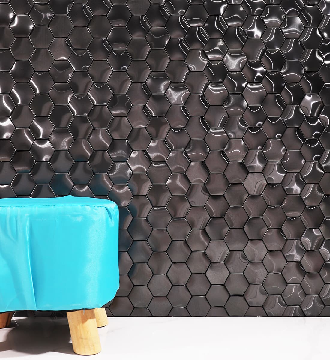 A wall decorated with black hexagon metal mosaic tiles behind a blue stool.