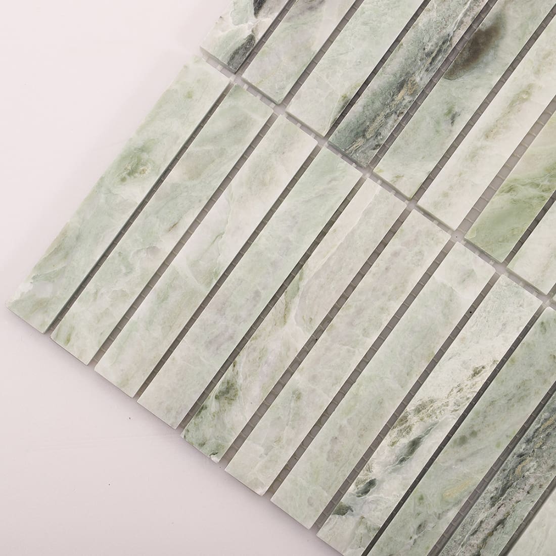 Edge closeup of light green marble mosaic sheet showing thickness and strip alignment