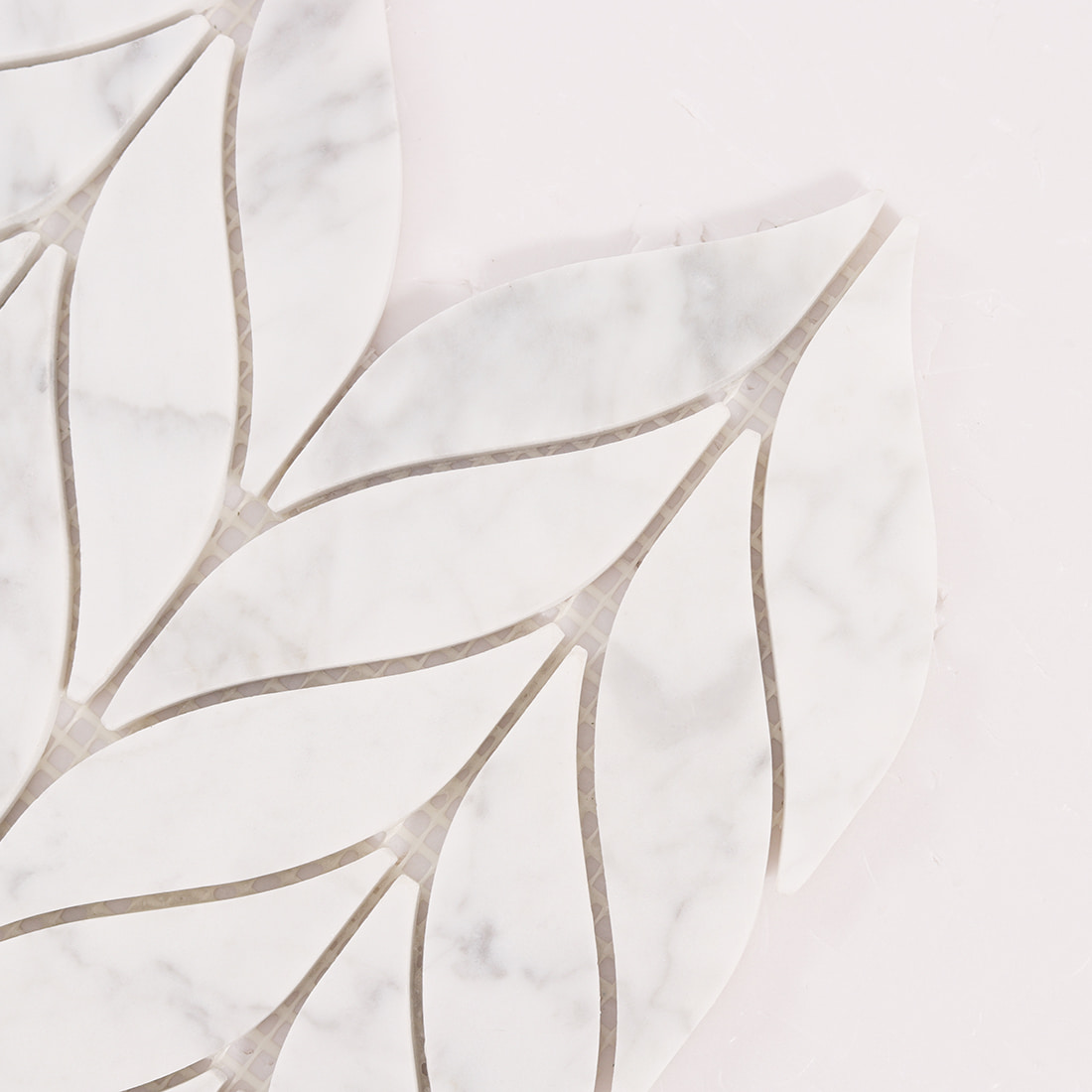 Close up of white marble leaf mosaic tiles showing curved edges and grout gaps