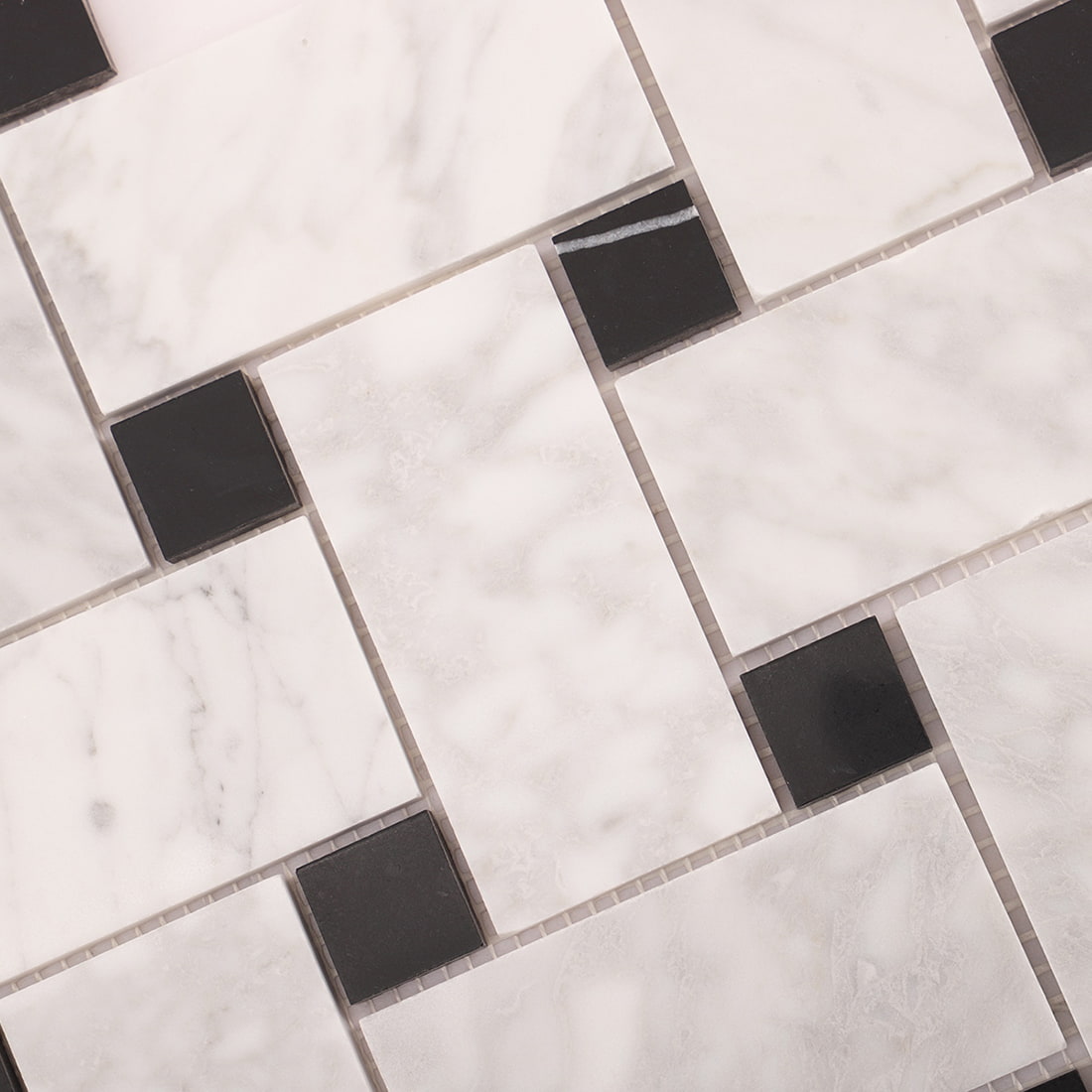 Macro of white marble rectangles with black square insets on a mosaic sheet.