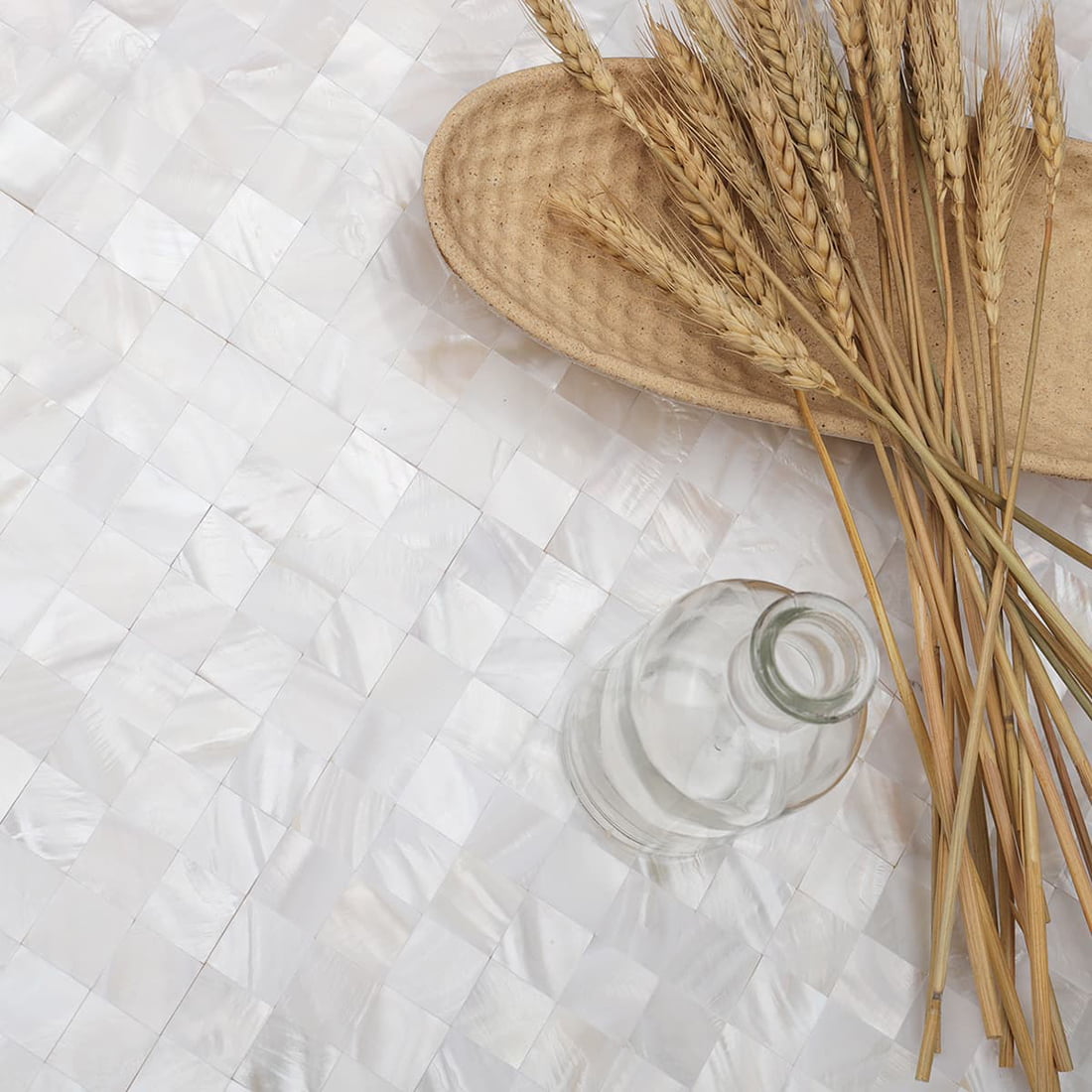 Styled scene on mother of pearl mosaic tile with wheat and glass bottle