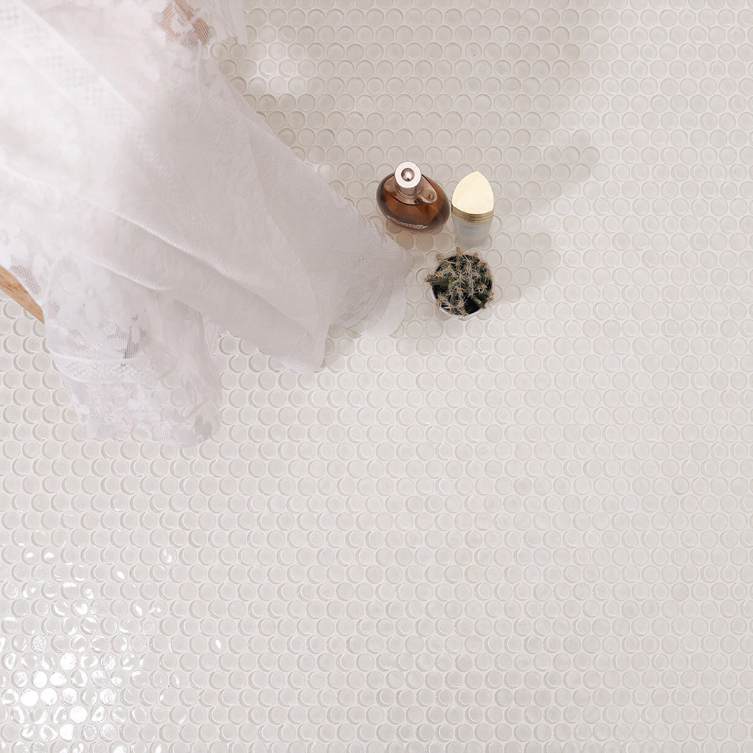 White round glass mosaic tile surface with a cactus, perfume bottle, and fabric.