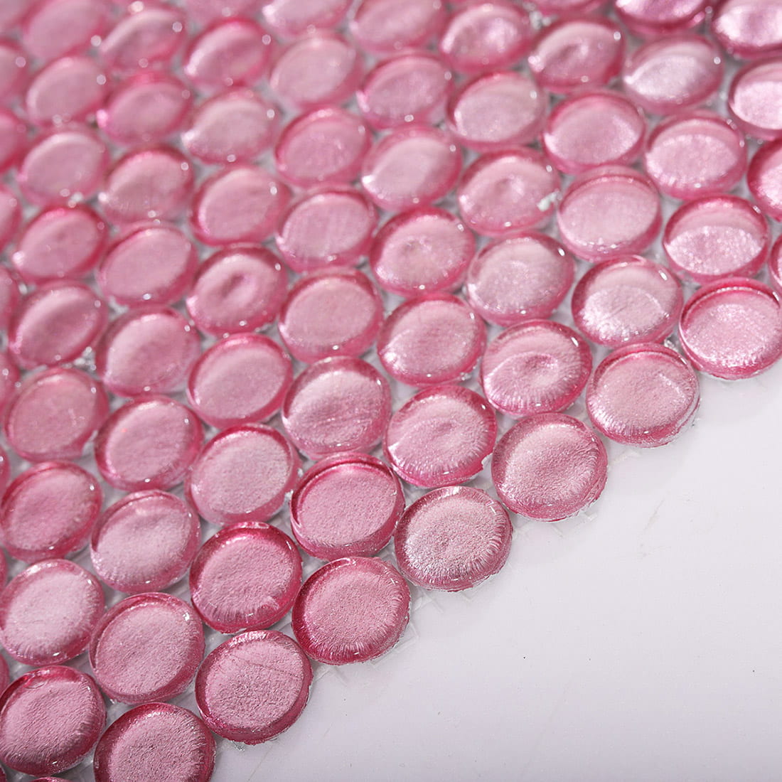 Angled view of pale pink penny round glass mosaic tiles showing glass depth