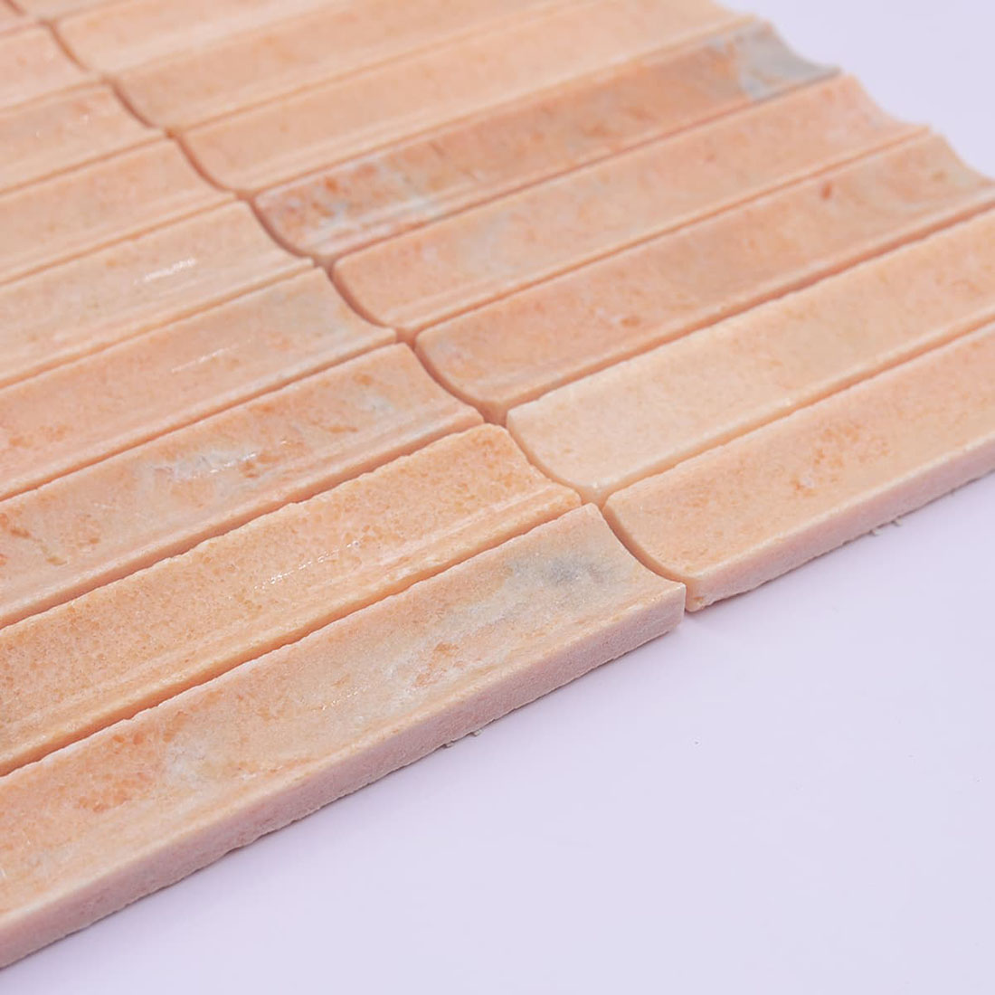 Angled close-up of peach stone strip mosaic showing thickness and grooved finish