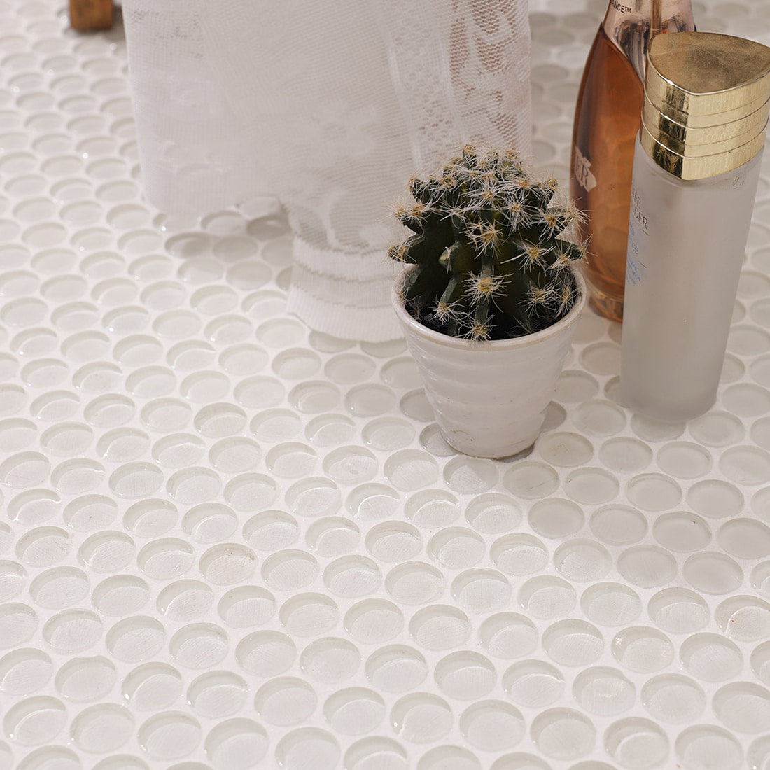 Perspective view of white penny round tiles styled with toiletries and a plant.