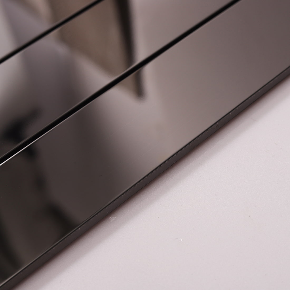 Side perspective of glossy black rectangle strip tiles on a white surface.