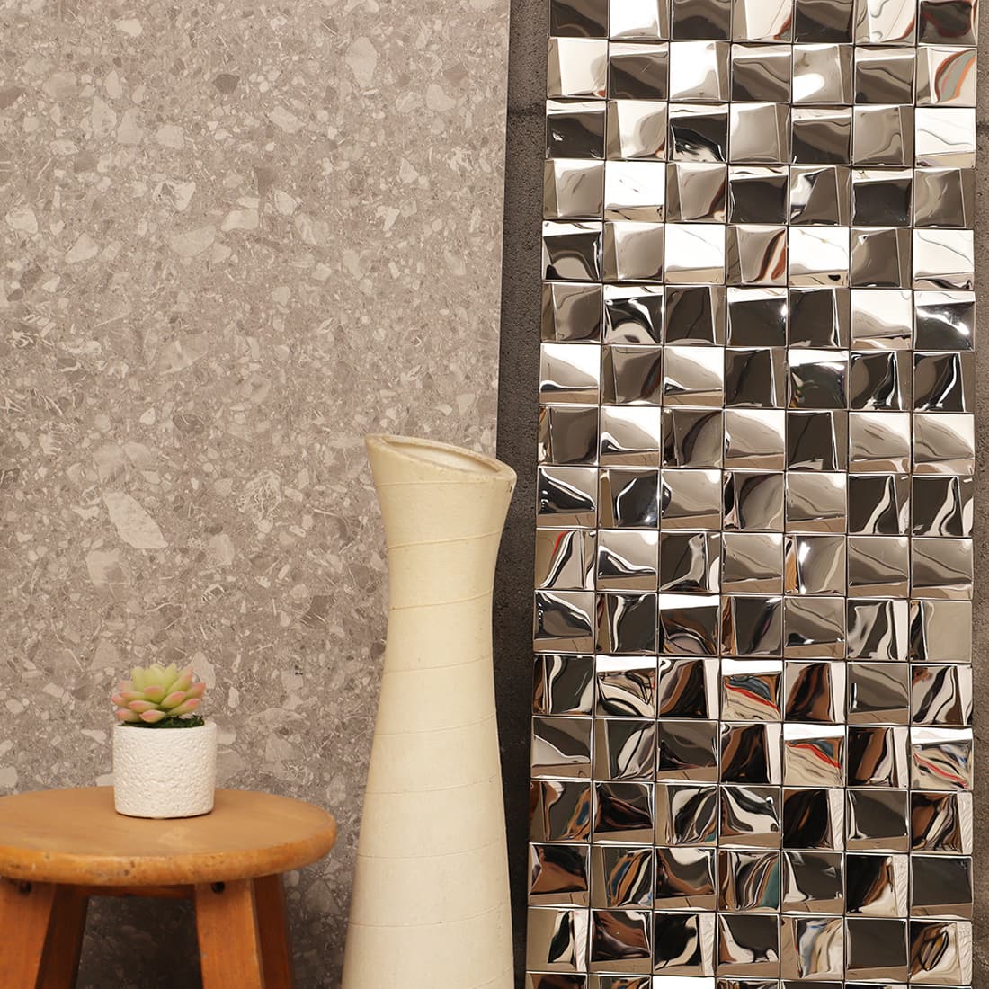 Modern interior decor featuring a silver 3D square mosaic tile wall next to a white vase.