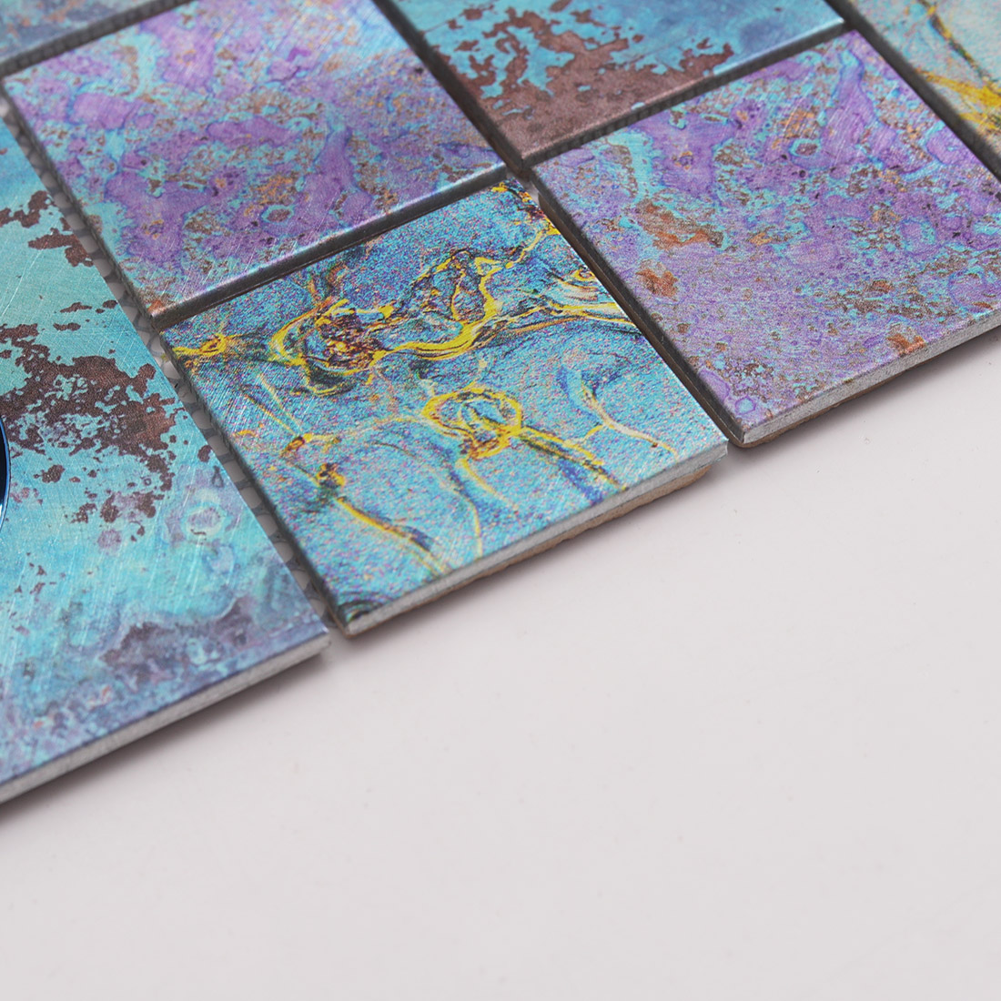 Edge detail of textured blue aluminum mosaic tile with iridescent accents