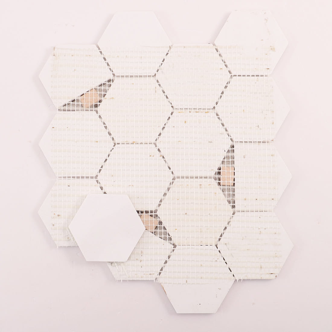 Back view of mosaic mesh backing with a loose white hexagon tile piece