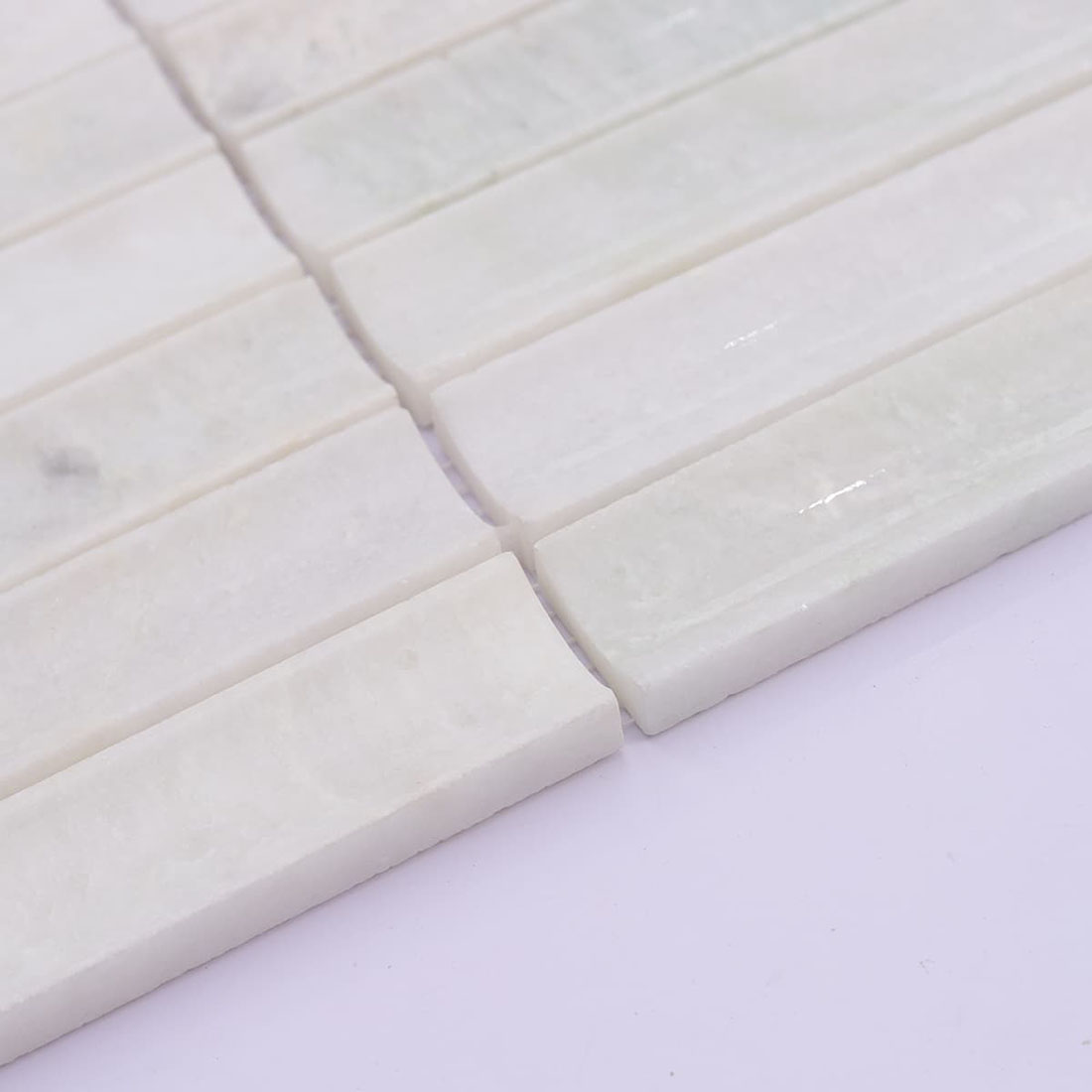 Angled view of white marble strip mosaic showing thickness and smooth edges