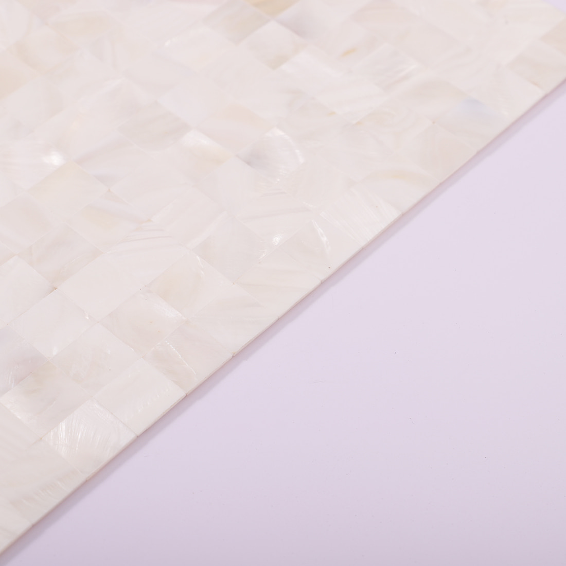 Angled edge detail of white mother of pearl mosaic tile sheet on lavender background