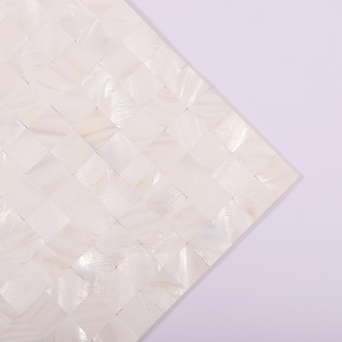 Corner view of white mother of pearl mosaic tile sheet on lavender background