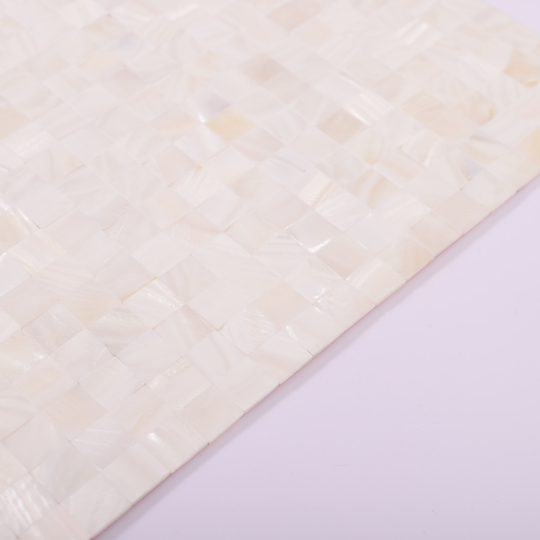 Angled edge detail of a white shell mosaic tile sheet on a lavender background