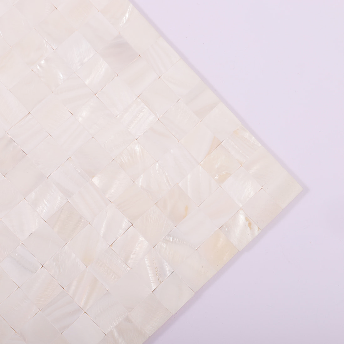 Corner view of a white shell mosaic tile sheet on a lavender background
