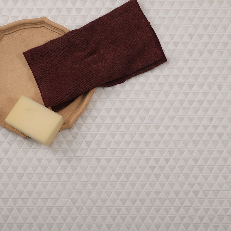 White triangle mosaic tiles with white grout beside a beige tray, soap and burgundy towel.