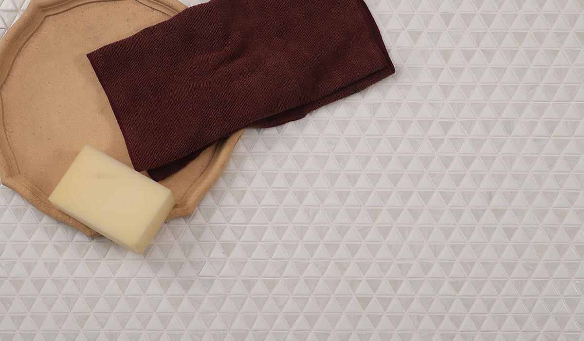 Wide view of white triangle mosaic tiles with a beige tray, soap and folded burgundy towel.