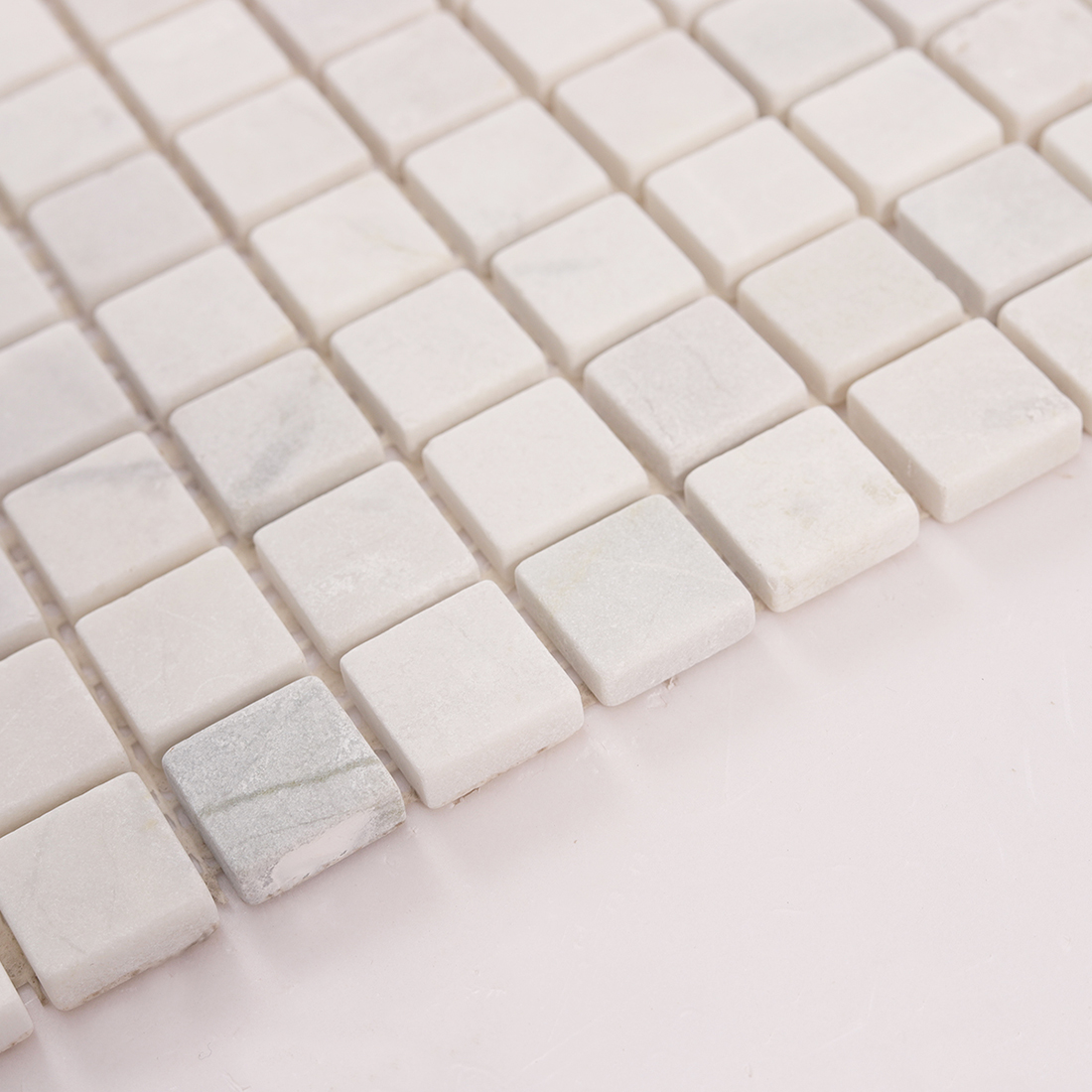 Angled view of white marble square mosaic tiles showing depth and grout lines