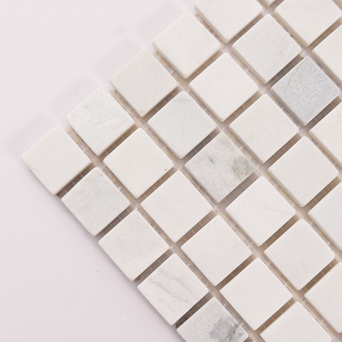 Diagonal detail of white marble square mosaic tiles showing stone variation