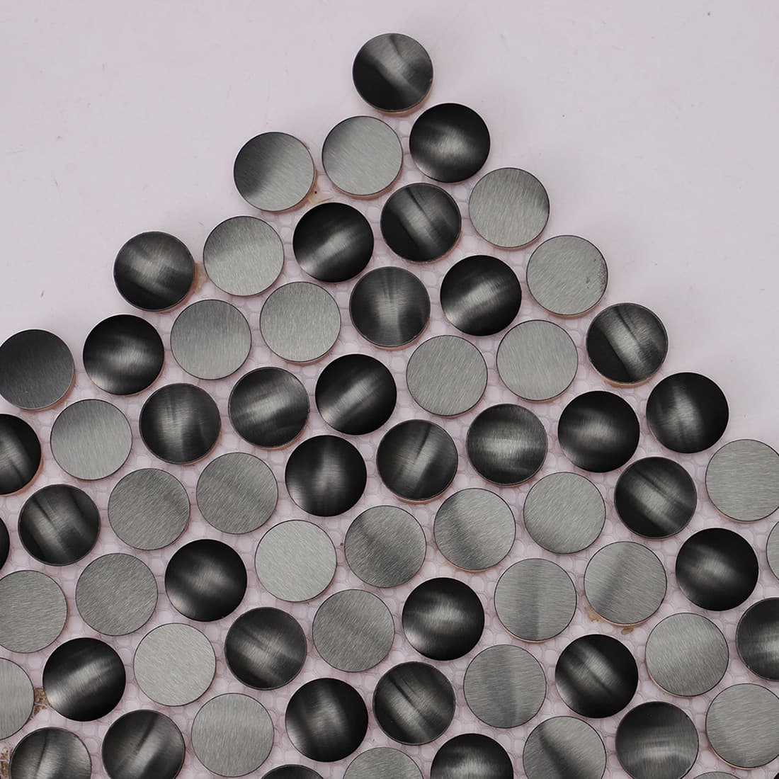 Angled view of black round stainless steel mosaic tile with brushed finish
