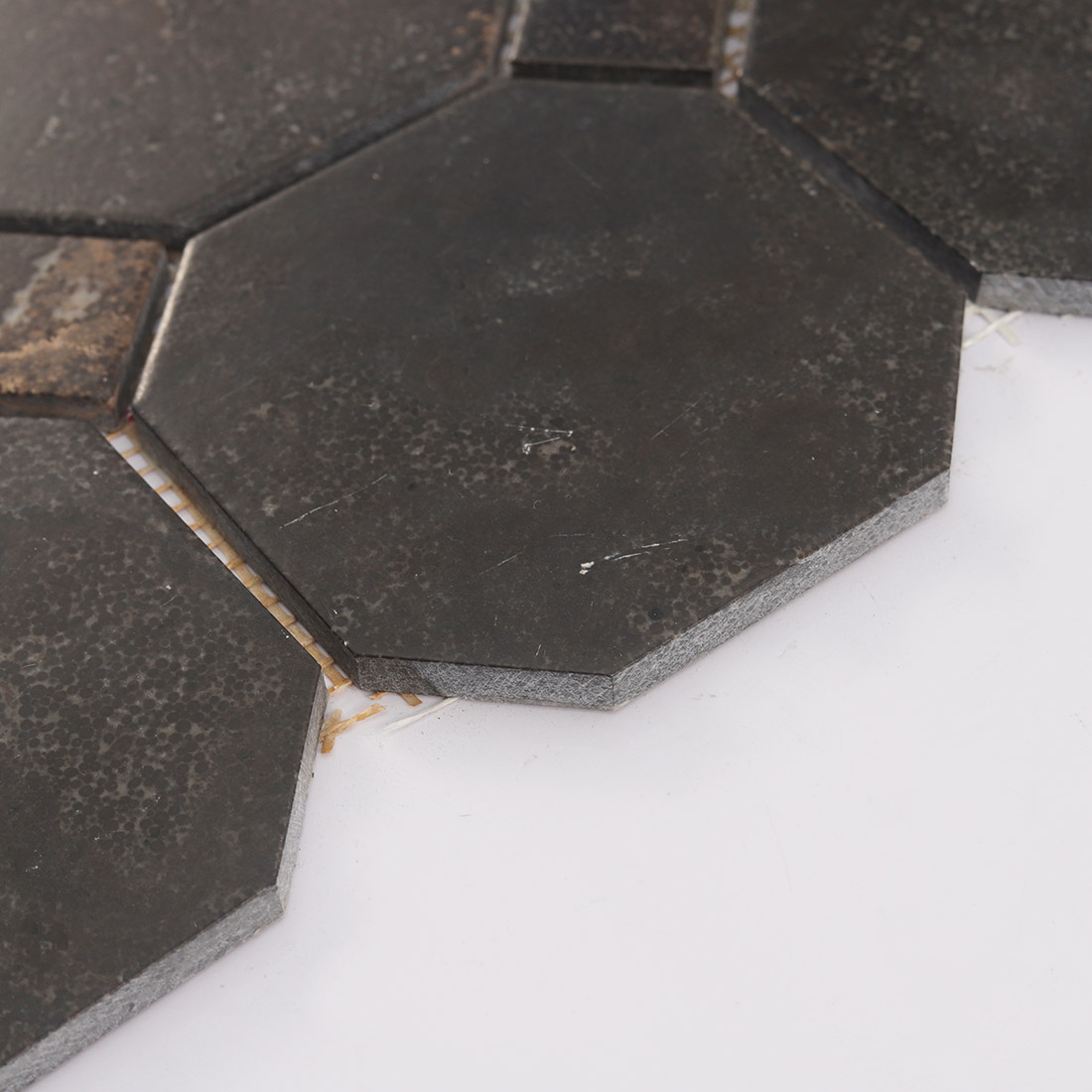 An angled close-up view showing the side edge texture of black brown octagon tiles.