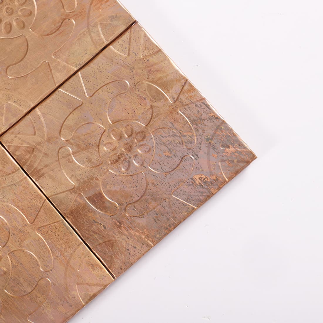 Corner detail of antique copper floral embossed square tiles