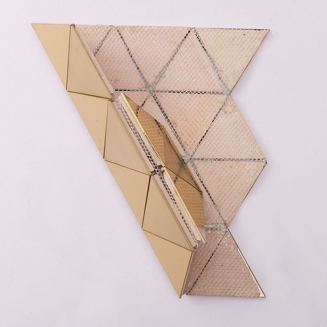 Back view of gold triangular metal mosaic tile showing the fiber mesh mounting.