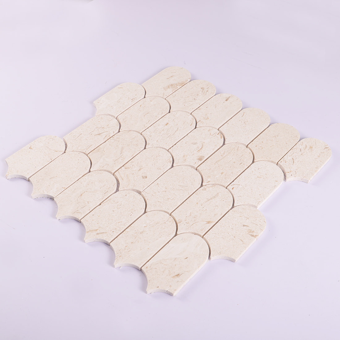 Angled display of beige marble scallop mosaic tile sheet