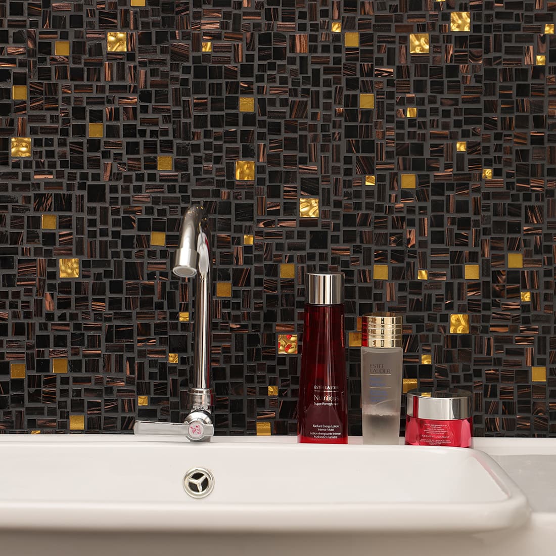 Black and brown mosaic backsplash with gold accents behind a white sink