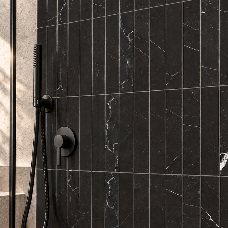 Close-up of black marble bathroom tiles with white veining and black shower fixtures