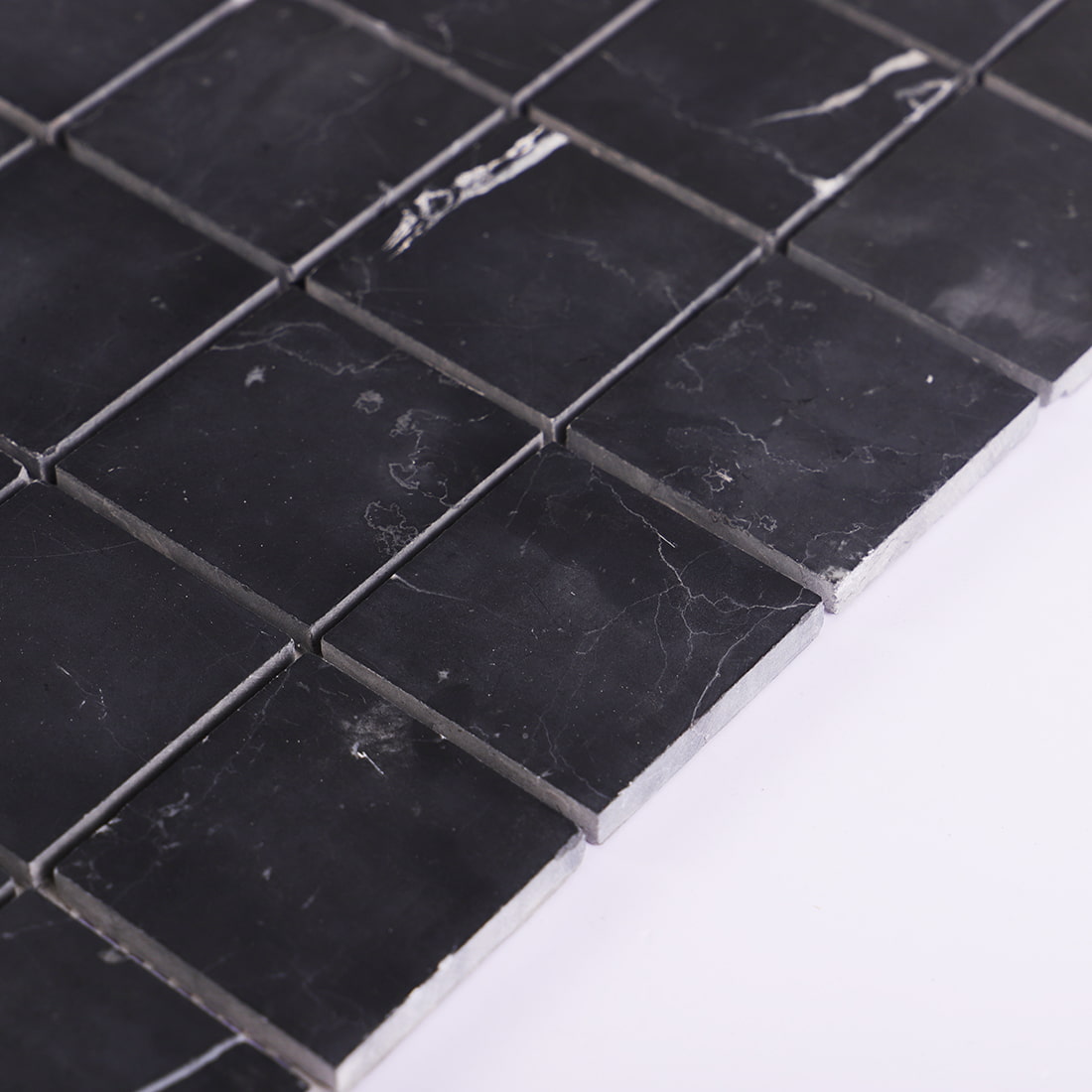 Angled edge view of black square marble mosaic tile showing tile thickness
