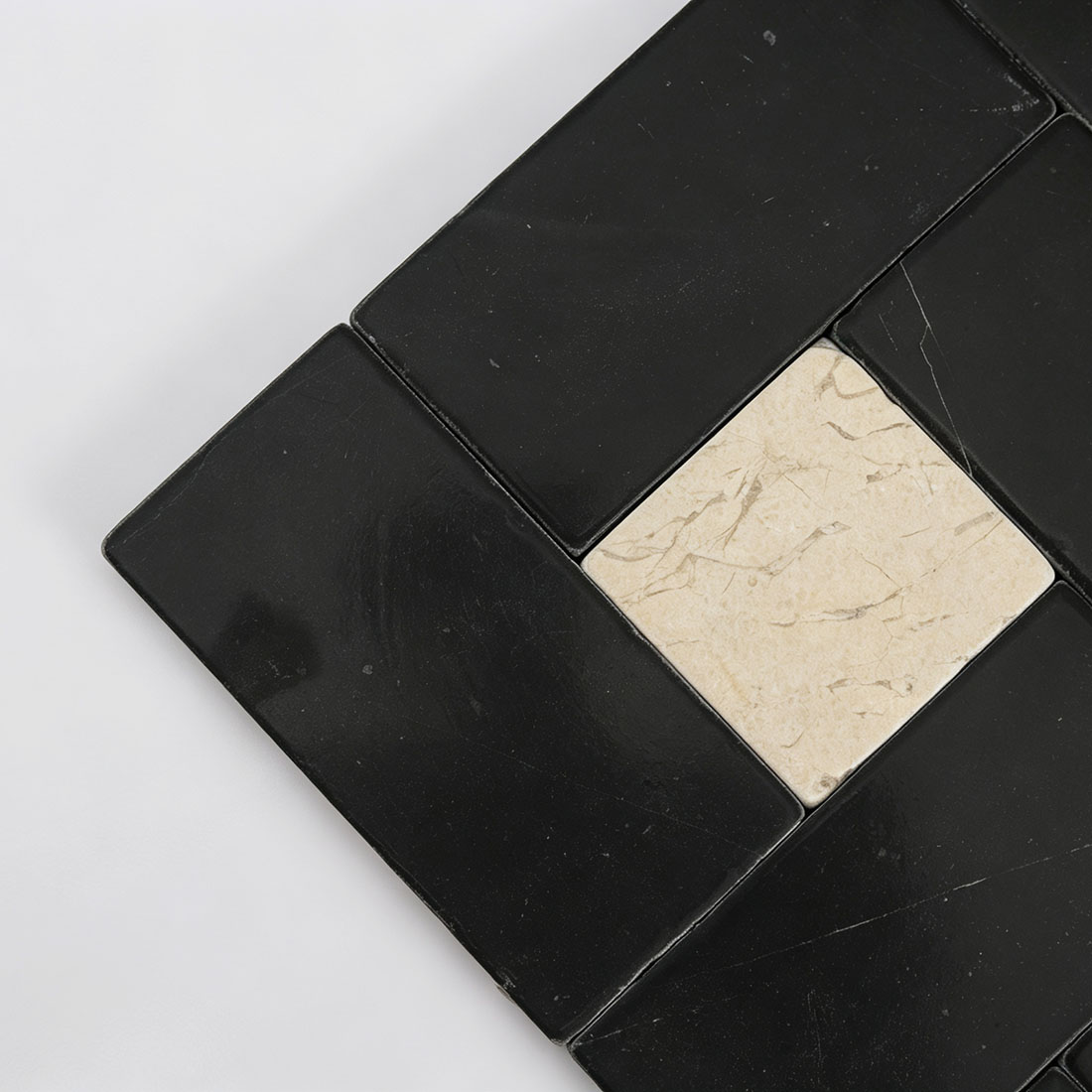 Close-up detail of beige travertine square accent on black marble