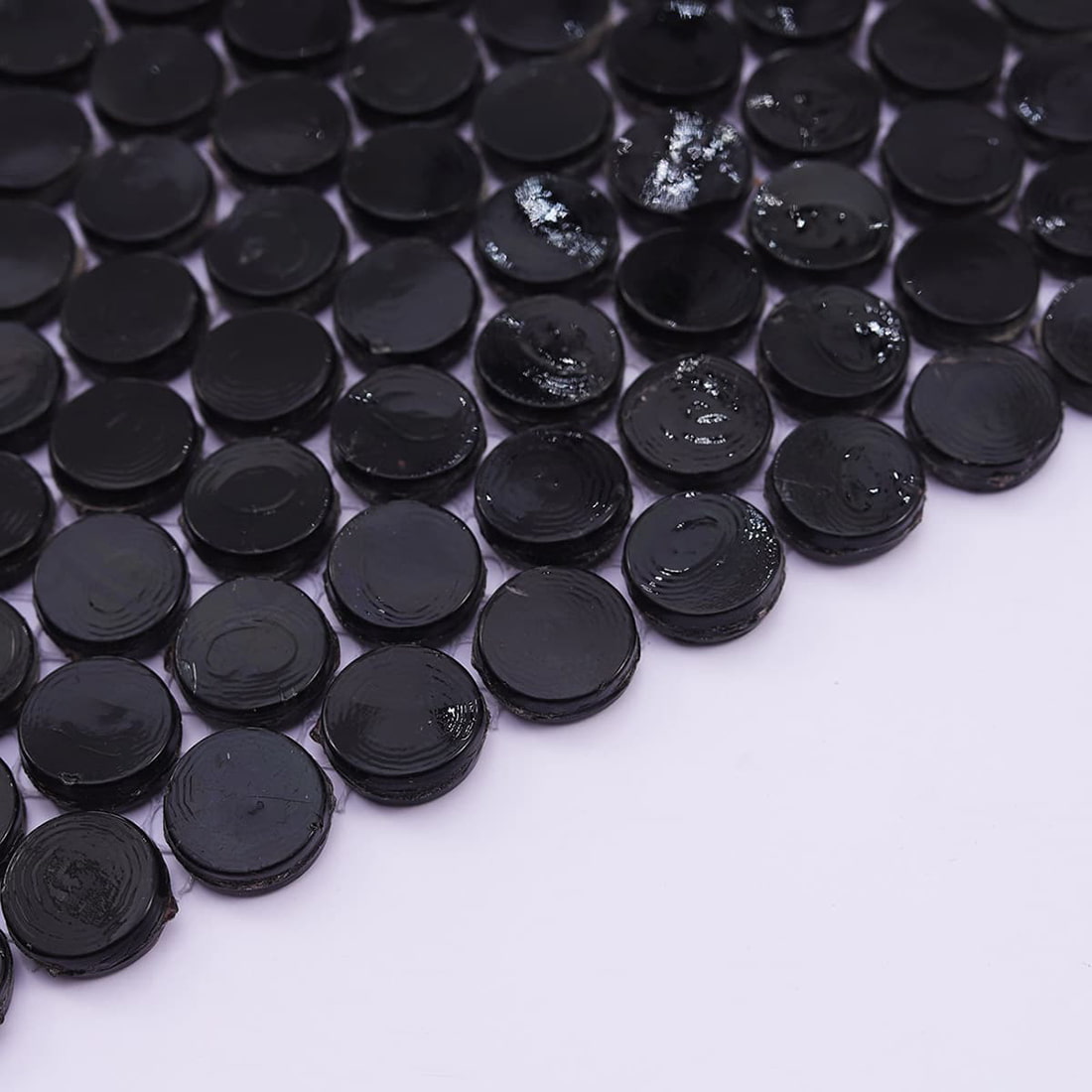 Detail shot of black glass penny tiles emphasizing the white fiber mesh backing.