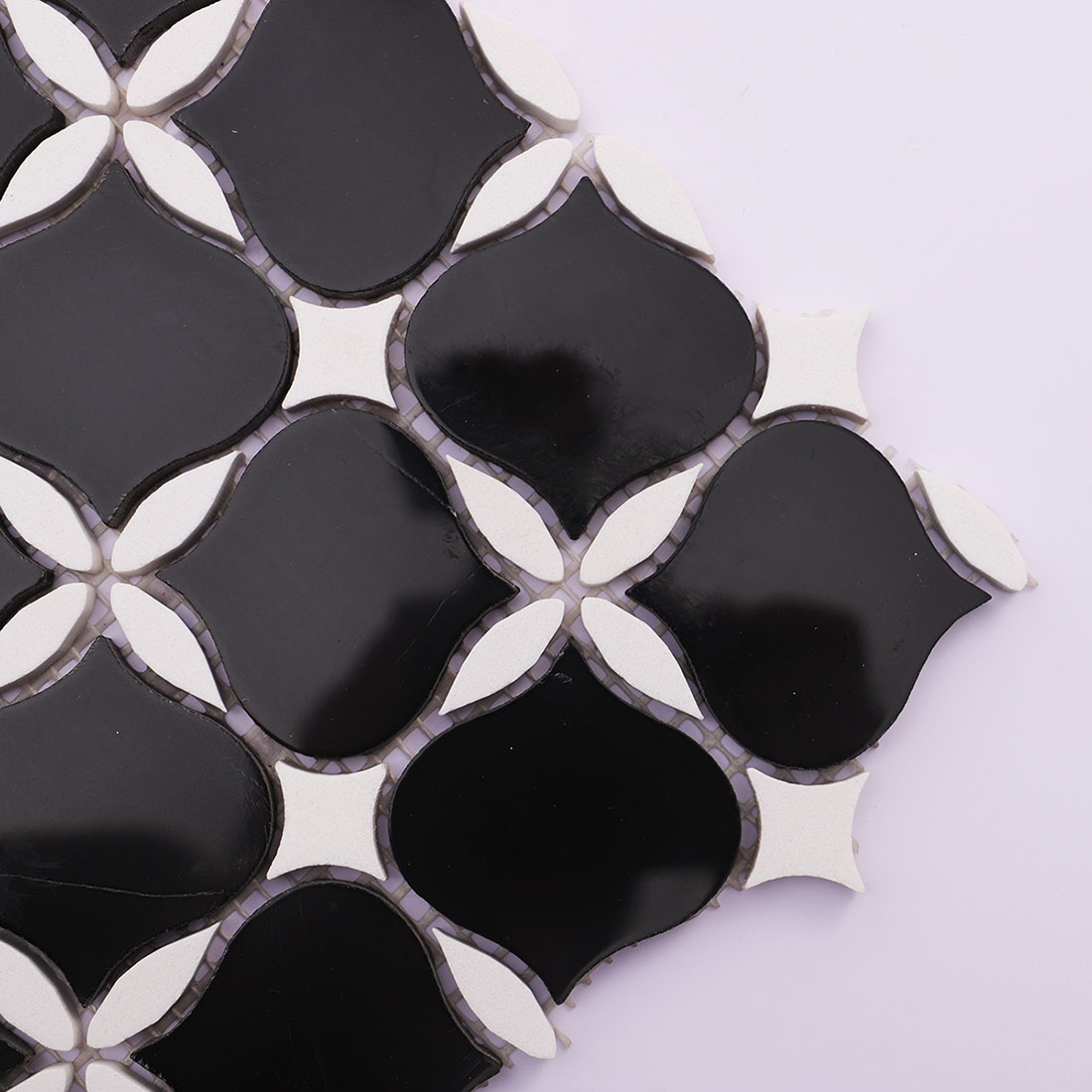 Black and white arabesque marble mosaic tile corner close-up with curved shapes.