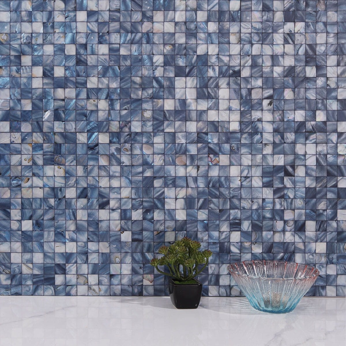 Blue shell mosaic tile wall with decorative bowl and small potted plant on a white countertop