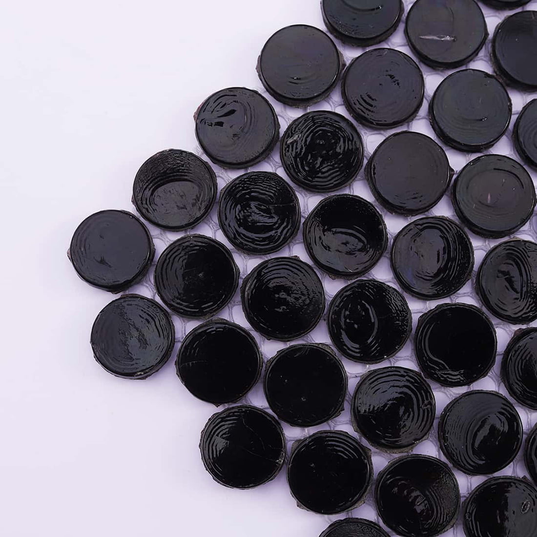 A macro shot showing the glossy finish and mesh backing of black round glass tiles.