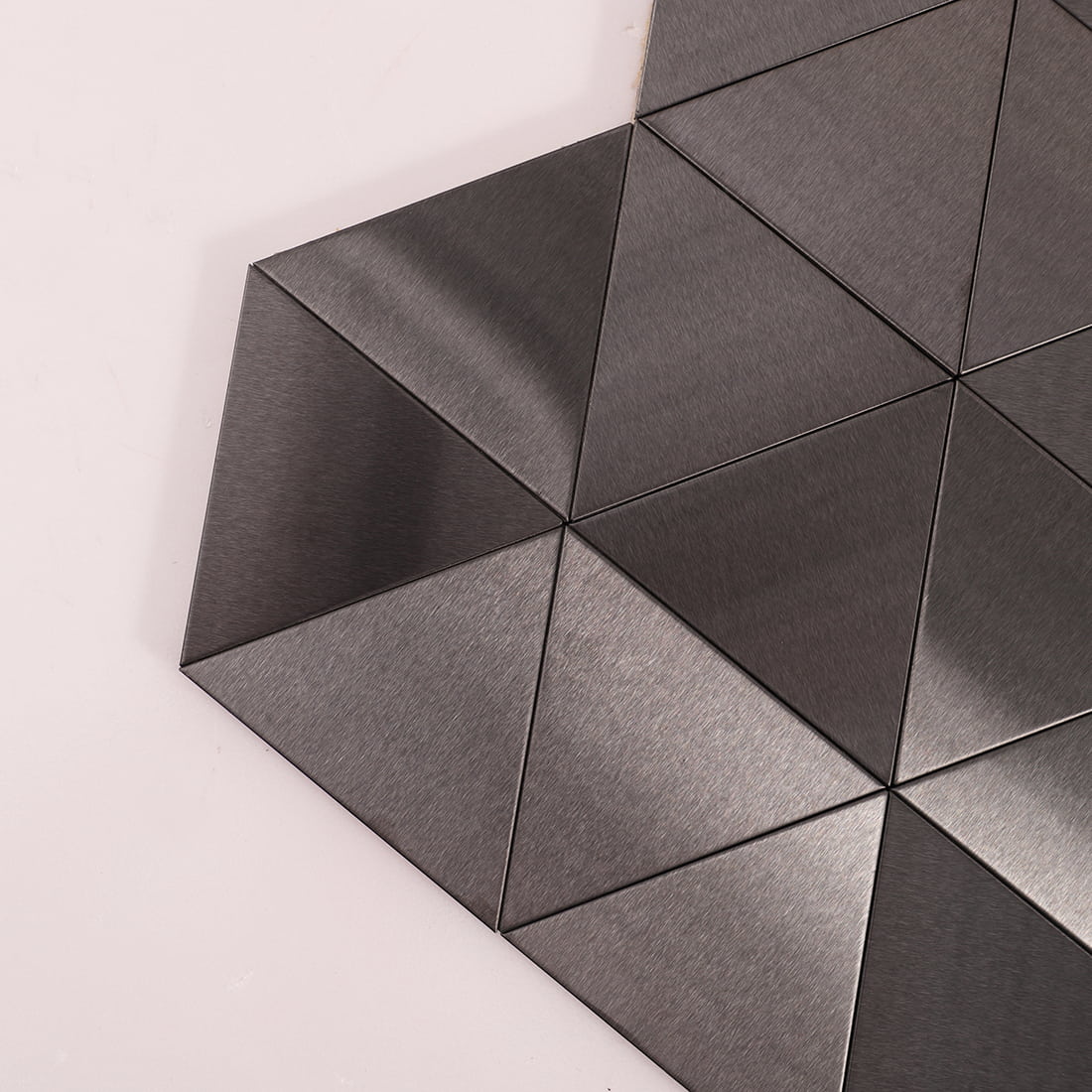 Close-up of brushed steel triangular tiles showing metallic grain and texture.