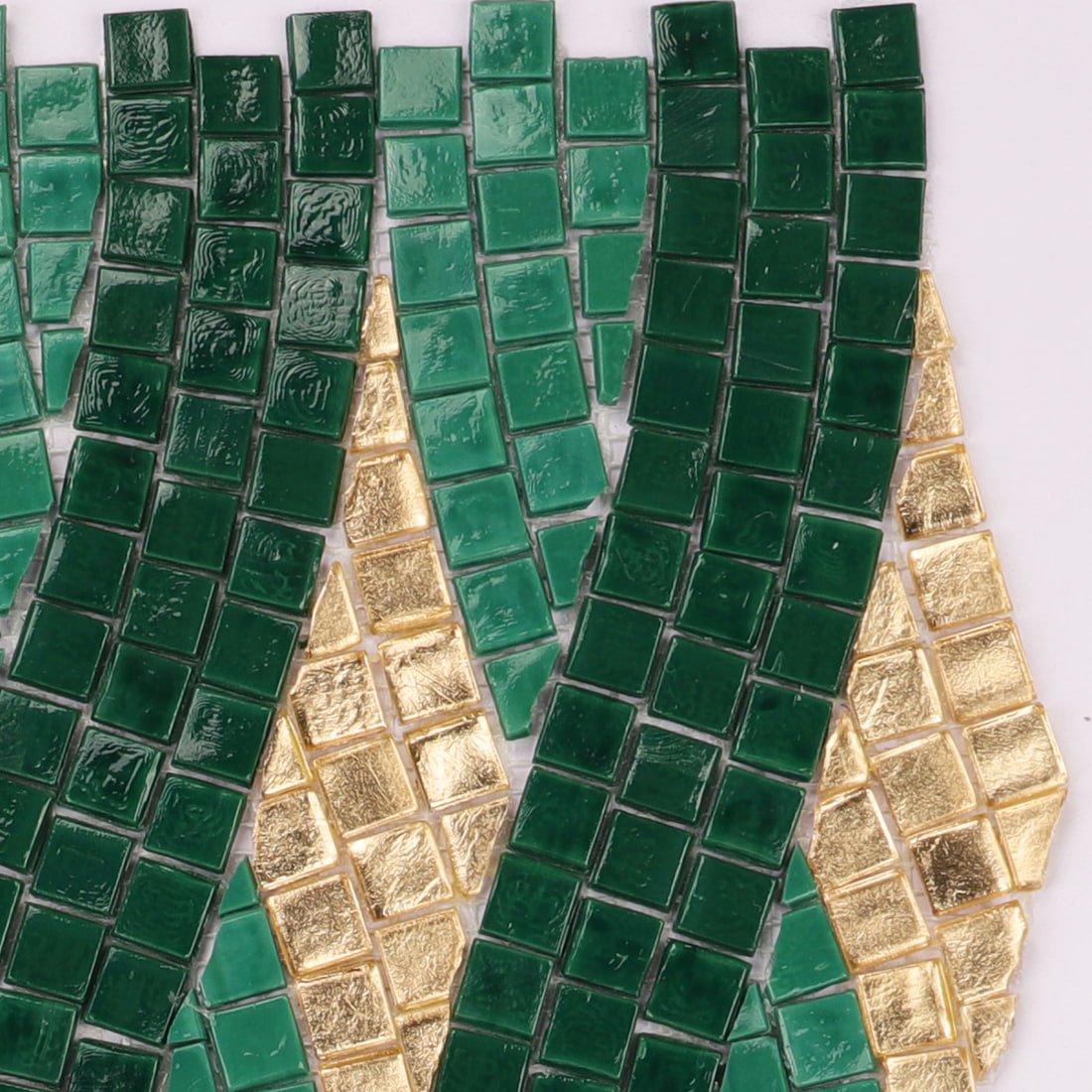 Close-up view of handmade glass mosaic tiles in green and gold rope pattern.