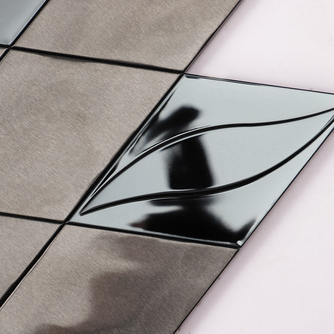 Close-up of a mirror black stainless steel diamond tile with a 3D wave leaf pattern.