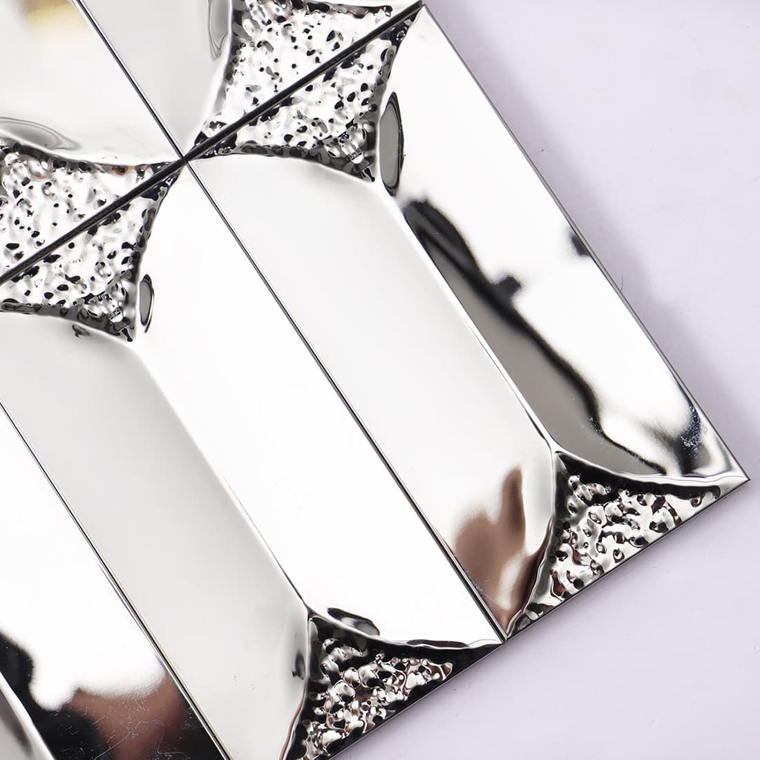 Angled close-up of reflective silver mirror 3D beveled metal tiles.