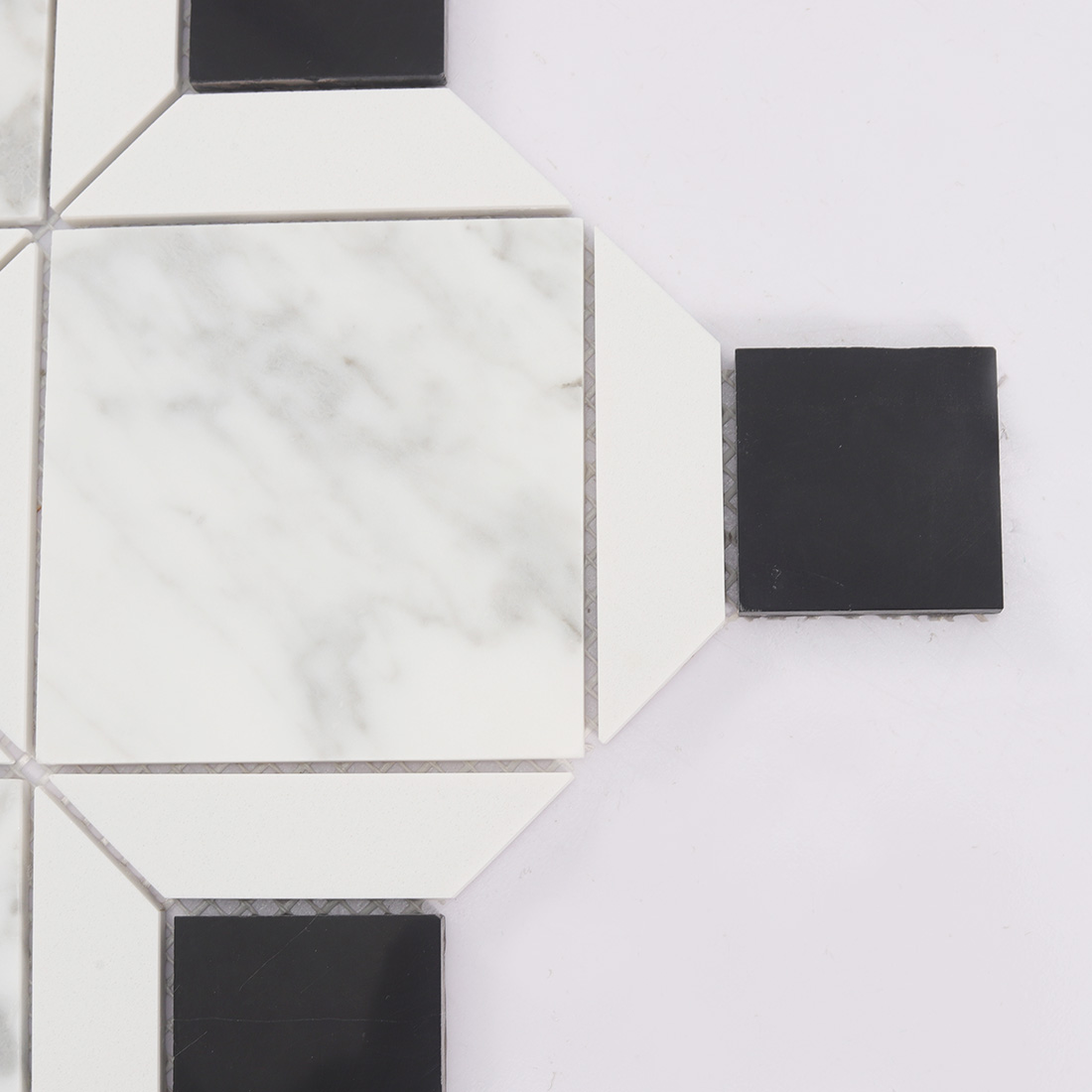 Close up of white diamond marble tile with black square insert and clean lines