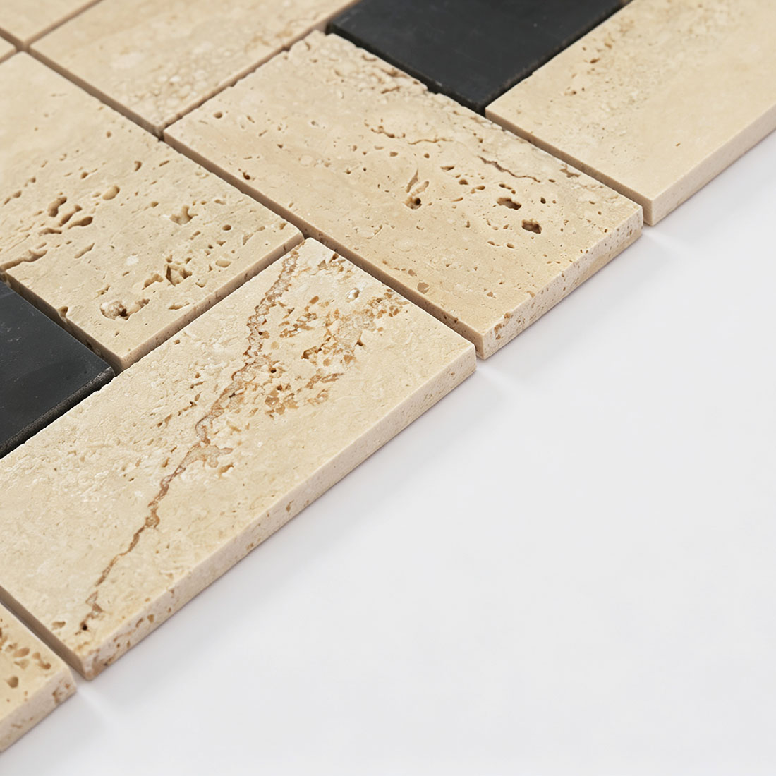 Edge profile of cream travertine and black stone tiles in a geometric mosaic sheet