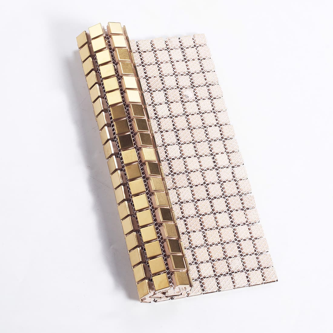 A gold mosaic tile sheet partially rolled to show its flexible white mesh backing.