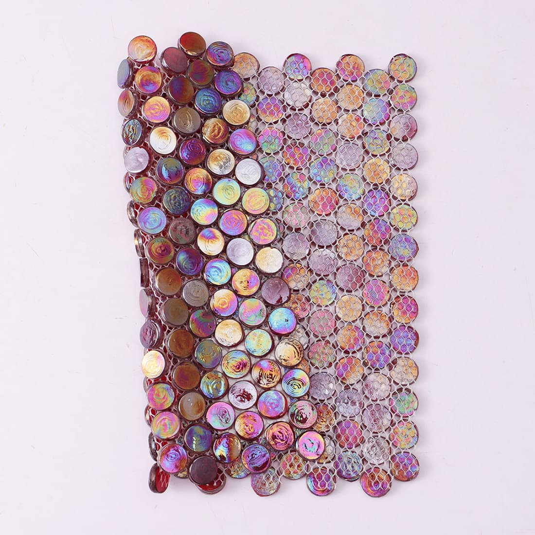 A partially folded sheet of red iridescent penny tiles showing the white mesh backing flexibility.