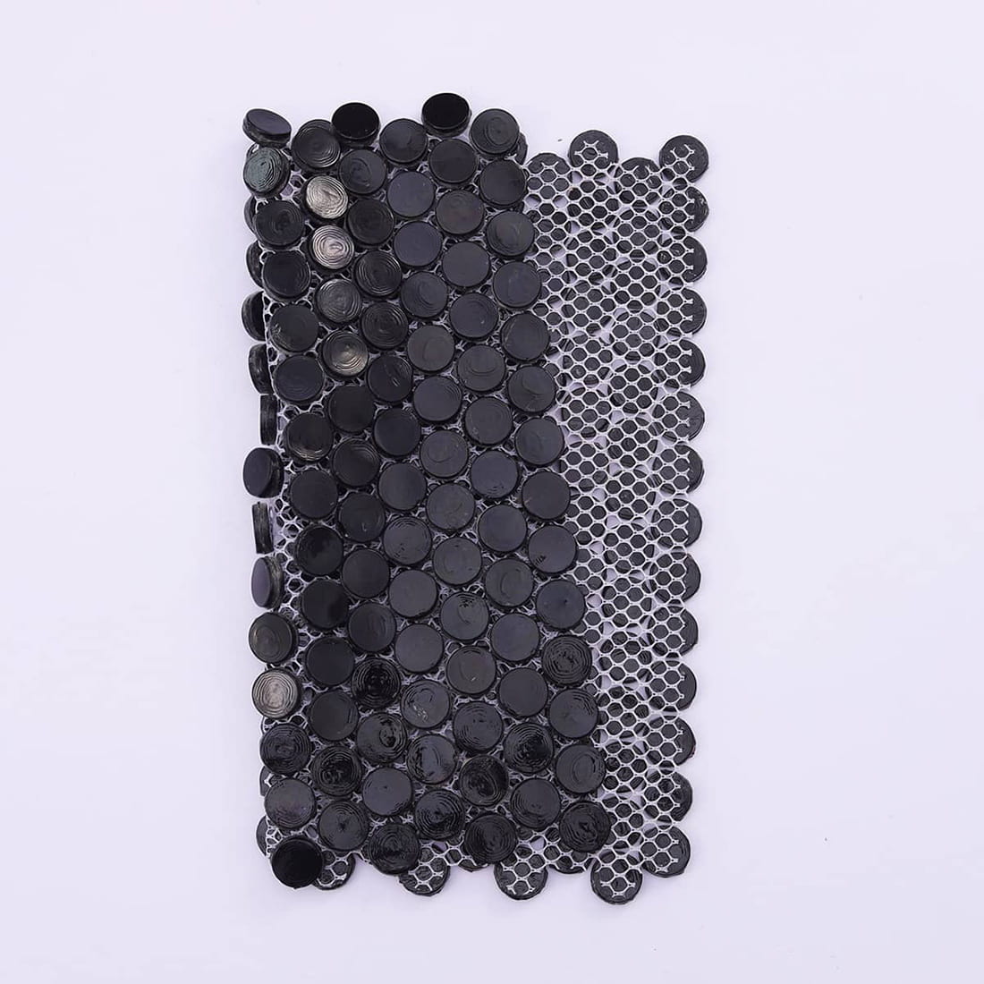 A folded sheet of black penny tiles showing the flexibility of the fiber mesh backing.