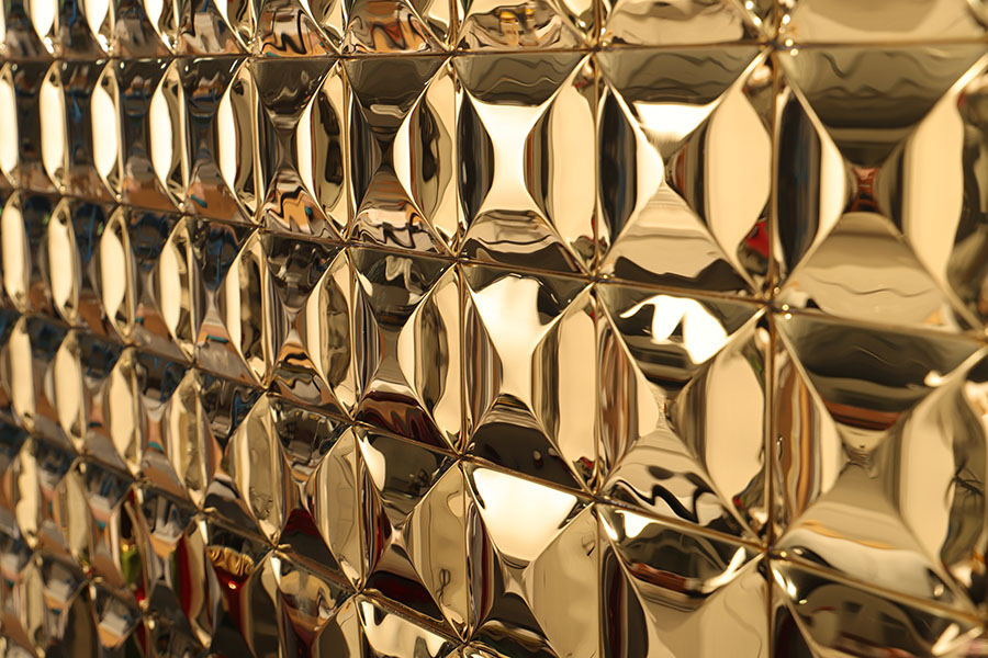 {"default":"Angled view of shiny gold 3D diamond metal wall tiles, showing depth and reflection"}
