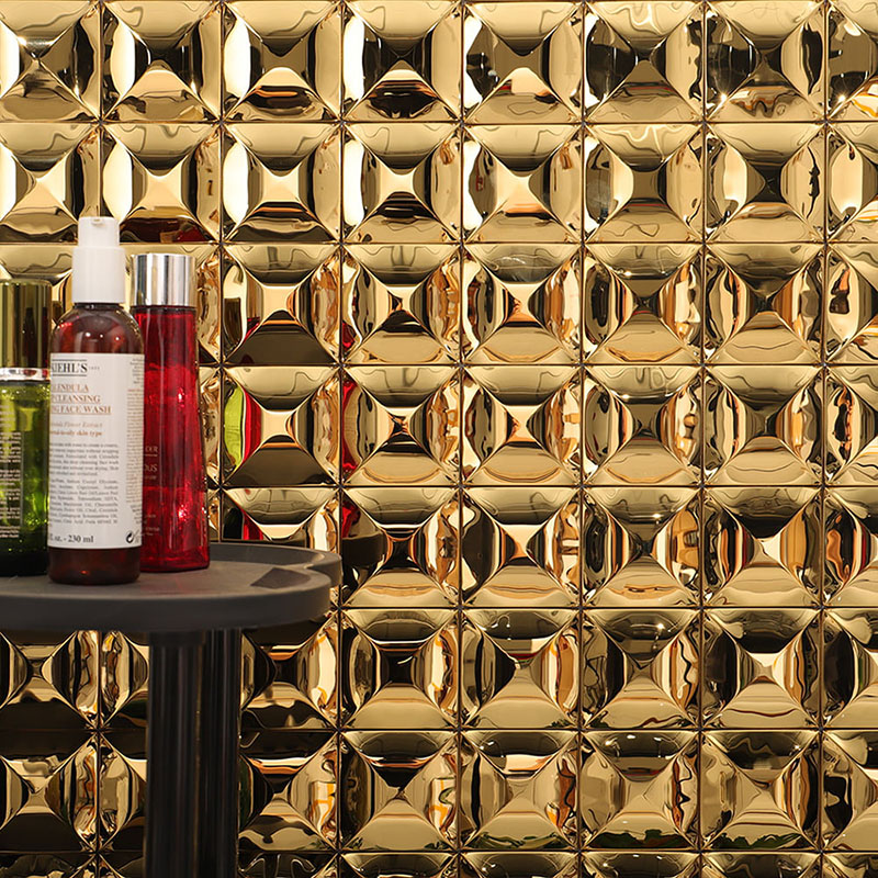 Gold mirror wall tiles with skincare bottles on a black round table