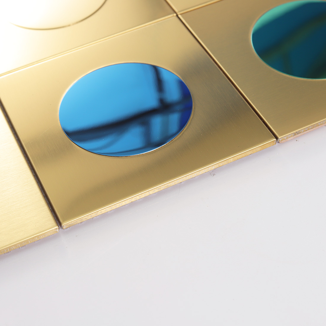Edge view of gold square metal tile with blue round mirror insert