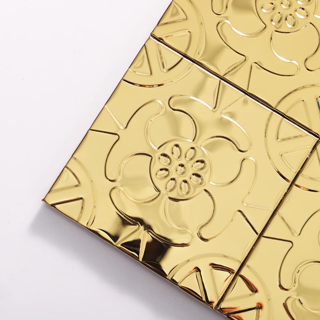 Corner detail of gold stainless steel floral embossed square tiles