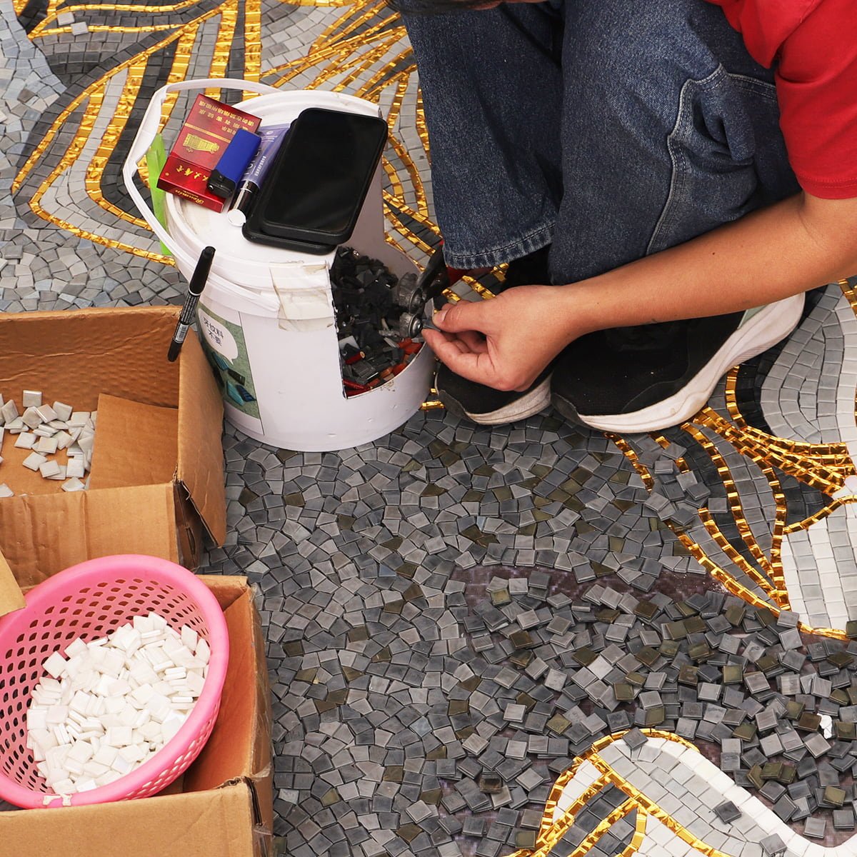 Artisan handcrafting golden mountain mosaic wall art using small tile pieces.